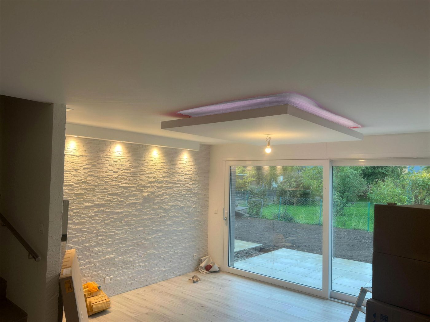 Séjour terminé : mur en pierre de parement blanche, faux-plafond avec spots et éclairage indirect, baie vitrée