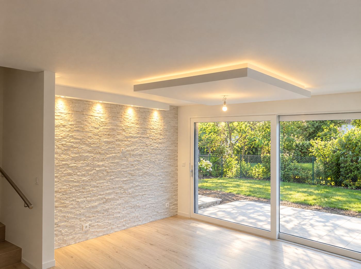 Séjour terminé : mur en pierre de parement blanche, faux-plafond avec spots et éclairage indirect, baie vitrée
