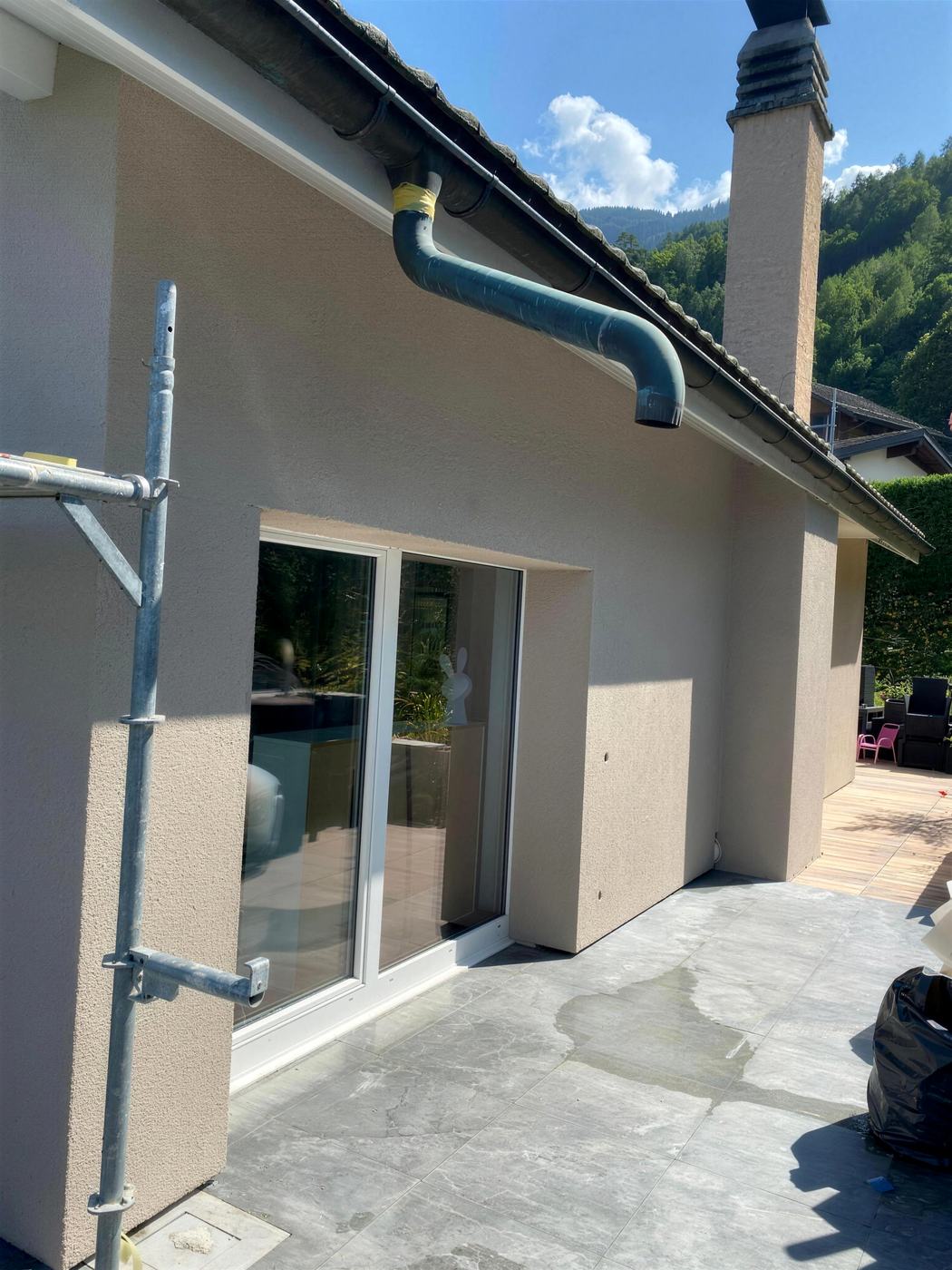Façade crépie avec baie vitrée et terrasse, collines derrière