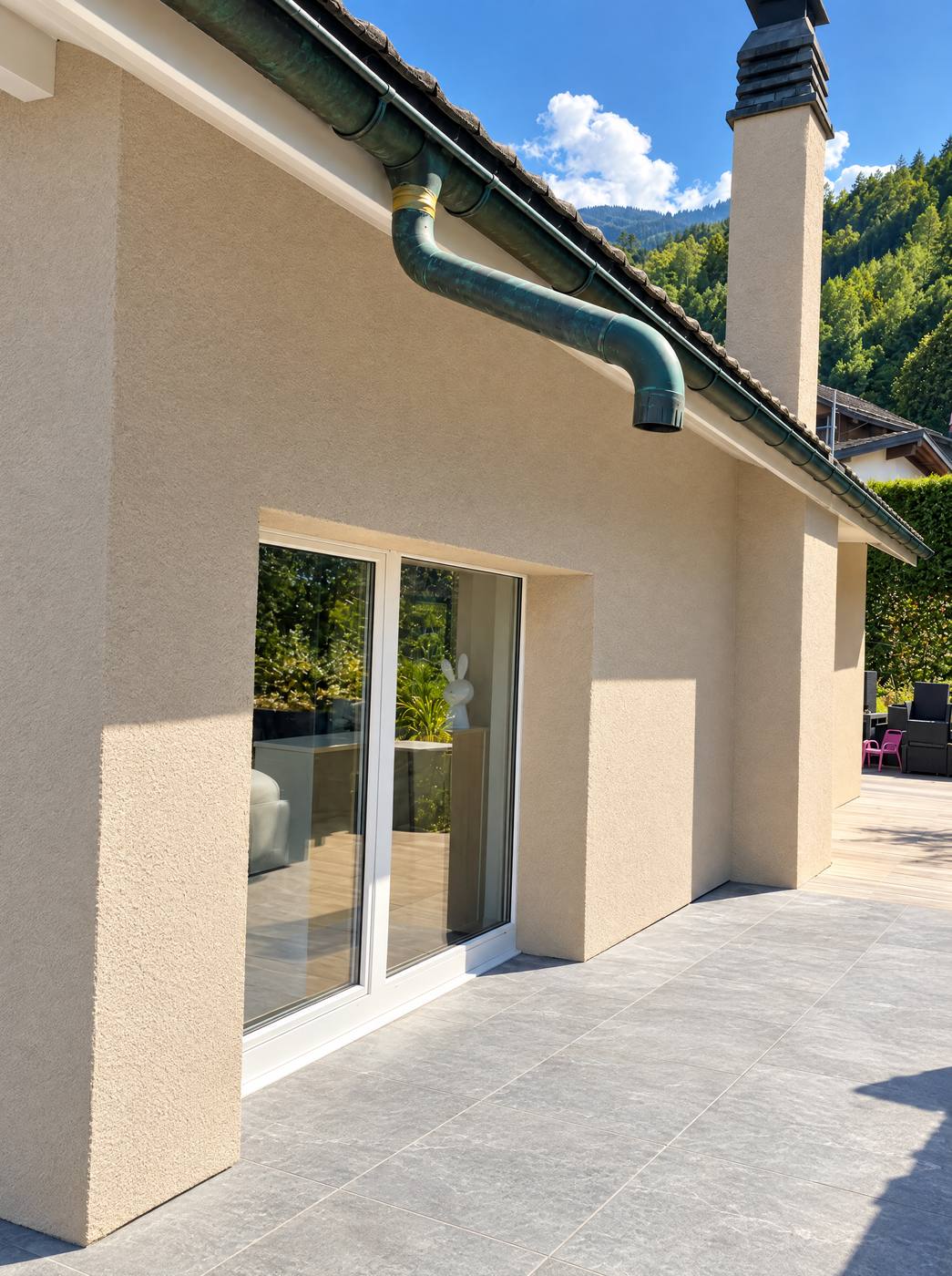 Façade crépie avec baie vitrée et terrasse, collines derrière