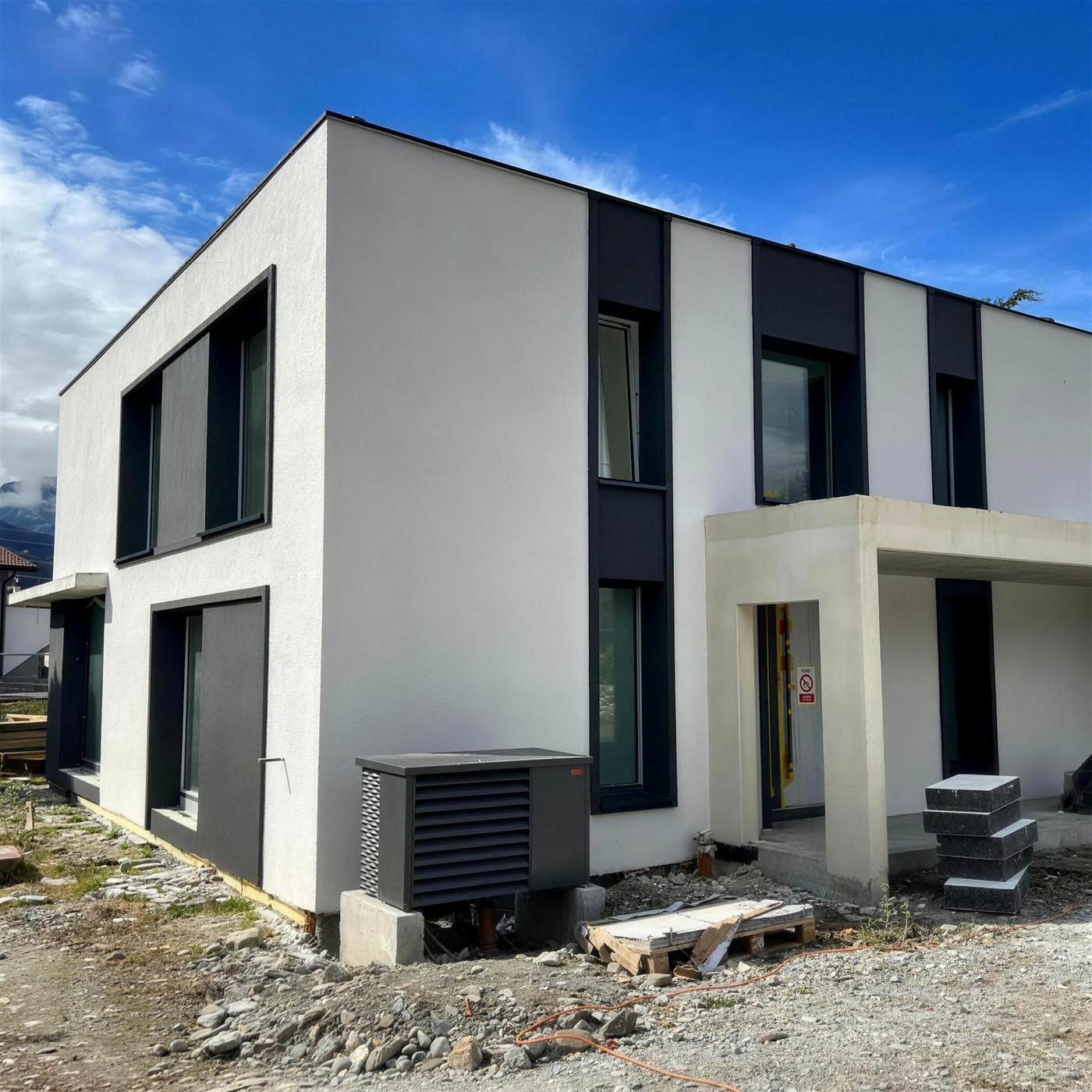 Maison neuve cubique, façade blanche et bandes anthracite, ciel bleu